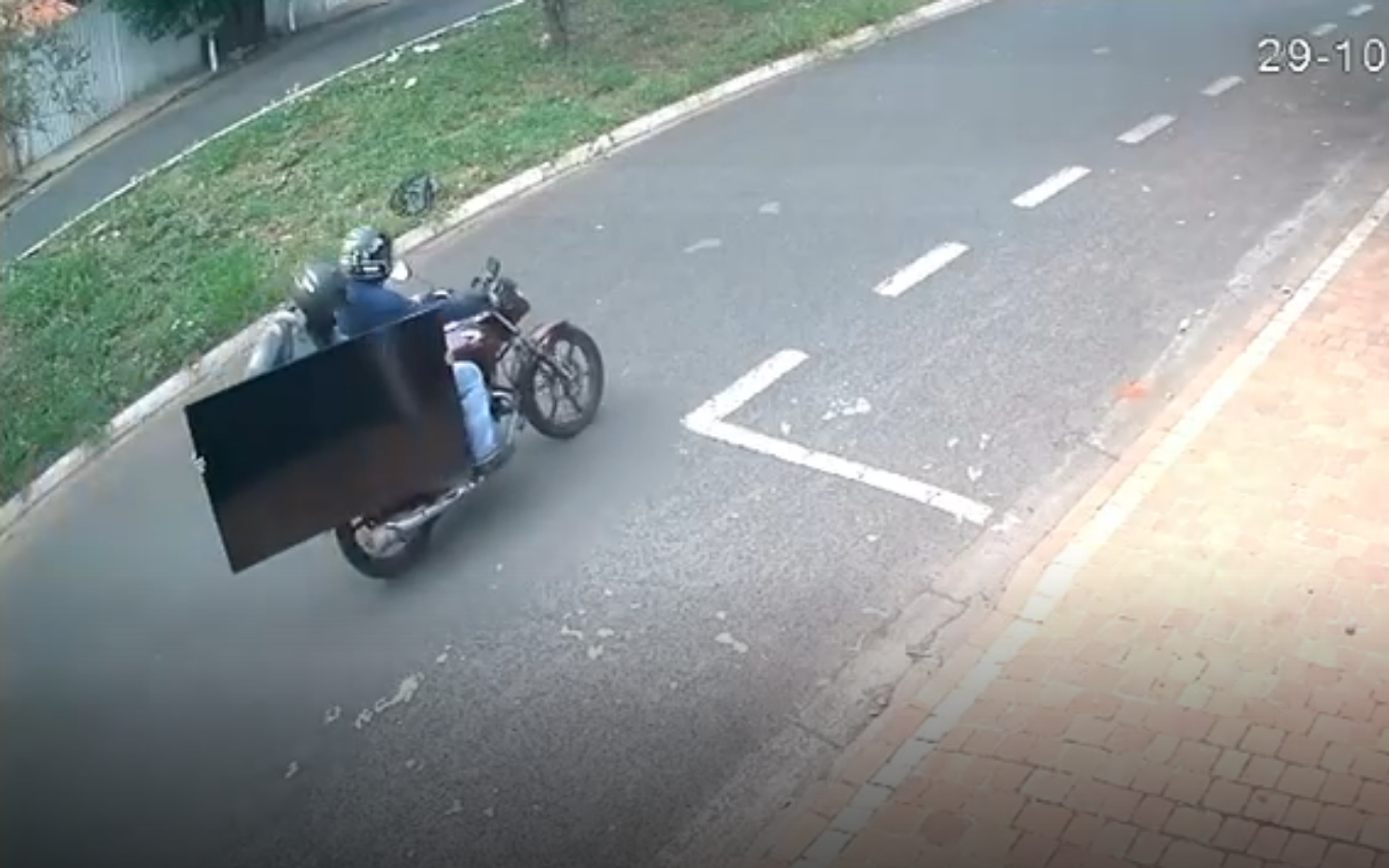 Flagra dos ladrões fugindo com uma televisão após o furto.